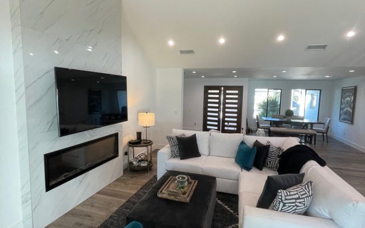 a beautiful luxury living room with a white couch, a wall-mounted television, carpeted floor and the dining area in the background